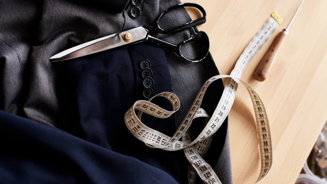 Une paire de ciseaux, un mètre ruban et un pantalon moderne disposés sur une surface claire.
