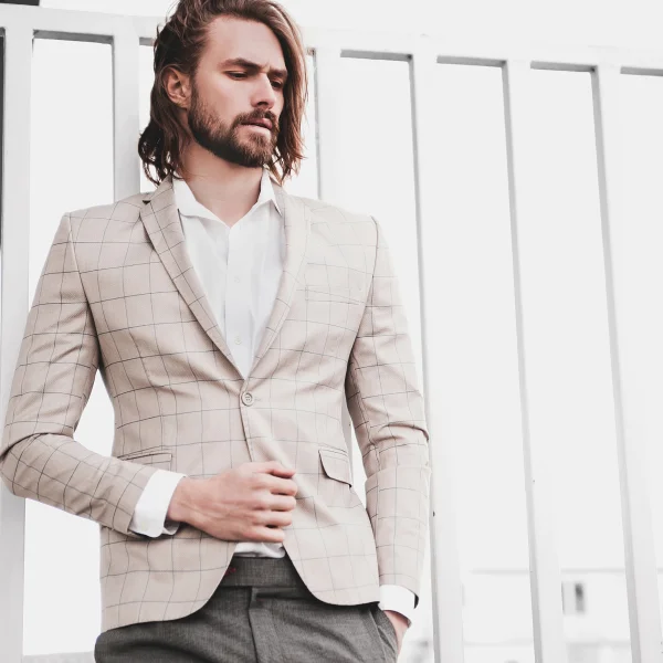 Un homme en costume et cravate se tient près d'un mur, affichant une tenue élégante pour un mariage.