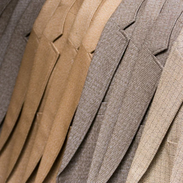 Une rangée de costumes de différentes couleurs, soigneusement alignés sur des cintres.