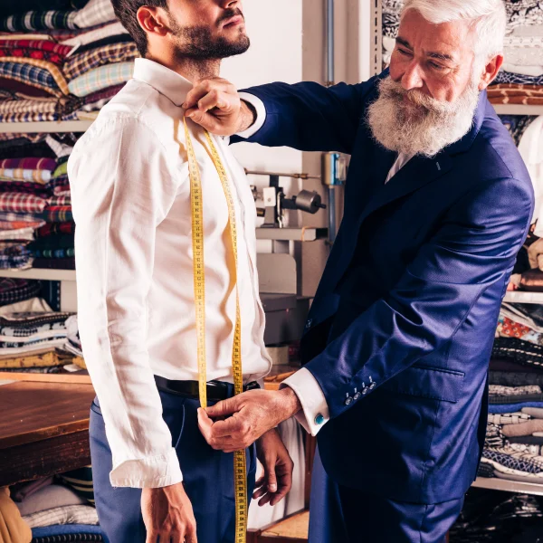 Un homme barbu en cravate mesure une chemise sur un autre homme dans un cadre moderne.