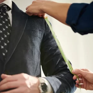 Un homme mesure un costume dans un atelier de tailleur luxe, prêt à ajuster les détails pour un ajustement parfait.