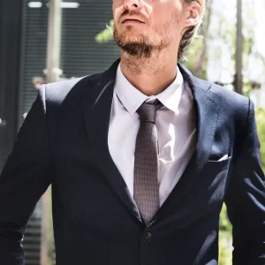 Un homme en costume et cravate se tient à l'extérieur, représentant un service de costume de mariage sur mesure.