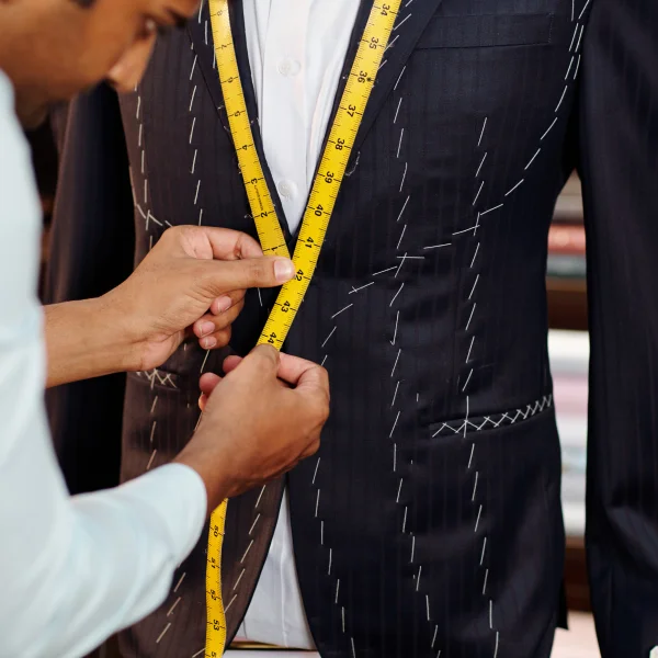 Un homme mesure un costume sur mesure avec un mètre ruban, concentré sur les détails de la coupe.