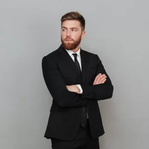 Un homme en costume et cravate se tient debout, les bras croisés, affichant une posture confiante.