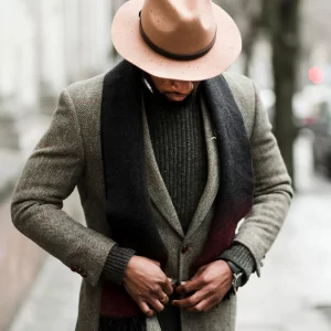 Un homme en chapeau et manteau se tient dans la rue, représentant le meilleur tailleur à Paris.