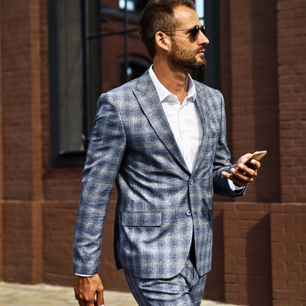 Un homme en costume et lunettes de soleil marche dans la rue, illustrant l'importance de la morphologie pour un bon ajustement.