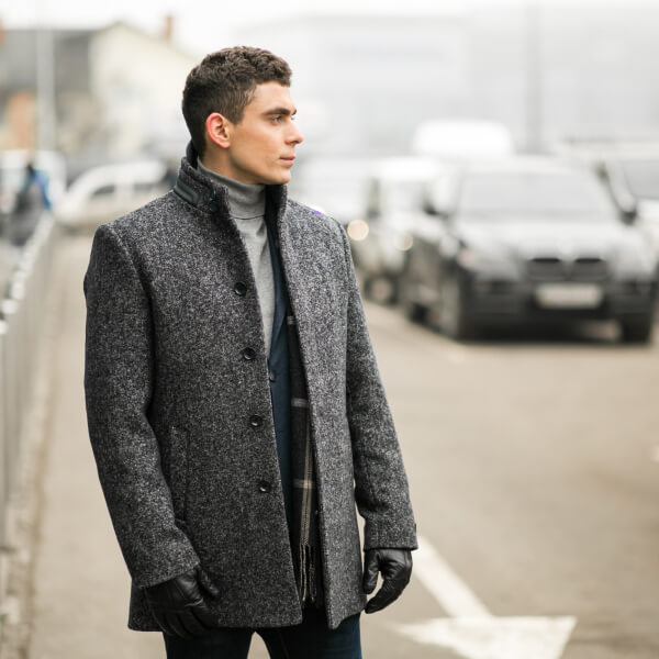 Un homme en manteau élégant et gants, se tenant sur la rue, incarnant le style masculin contemporain.