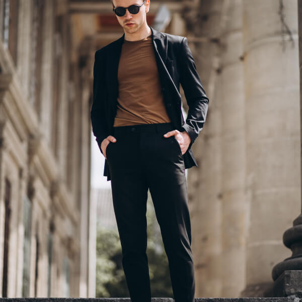Un homme en costume et lunettes de soleil se tient sur des marches, illustrant l'élégance du sur mesure dans le vestiaire masculin.