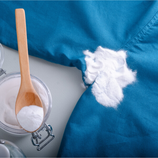Bicarbonate de soude appliqué sur un tissu bleu pour nettoyer naturellement les taches de col de chemise