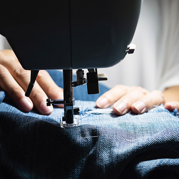 Travail de couture sur tissu bleu en atelier, illustrant le temps nécessaire pour fabriquer un costume sur mesure de qualité.