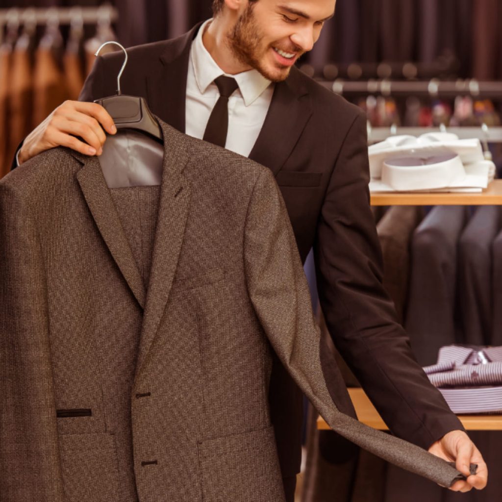 Homme souriant tenant une veste de costume en boutique, illustrant la confiance d’un candidat bien préparé pour un entretien d’embauche.