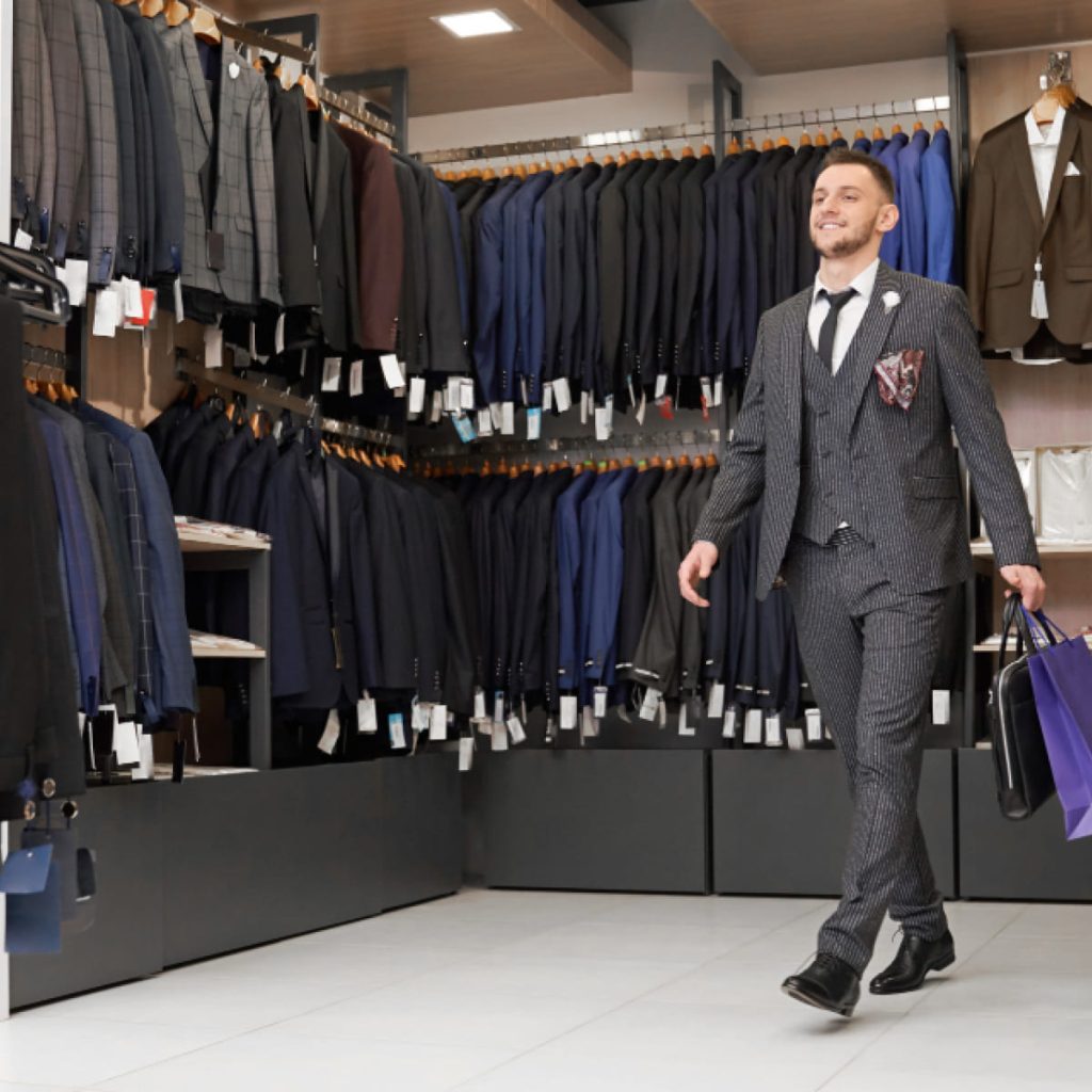 Homme en boutique de costumes professionnels comparant différentes coupes et matières pour choisir un tissu adapté au travail.