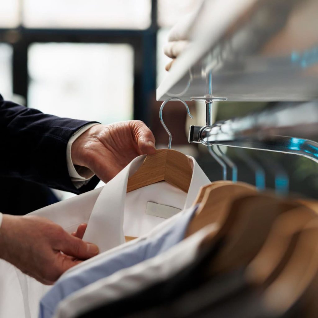 Main choisissant une chemise sur cintre en boutique, illustrant le choix des tissus et matériaux pour une tenue d’entretien d’embauche soignée.
